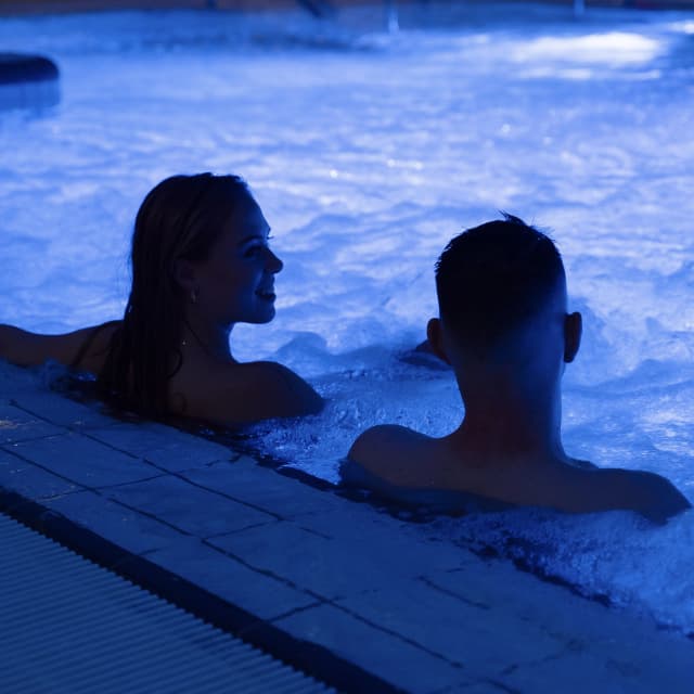 Paar sitzt abends im beleuchteten Whirlpool des Hains Freizeitzentrums Freital und genießt die entspannte Atmosphäre