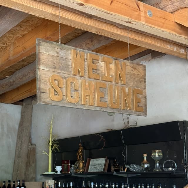 Holzschild mit Aufschrift „Weinscheune“ über einer Theke im Innenbereich von Friebels Weinscheune in Radeburg, umgeben von Gläsern und Weinflaschen